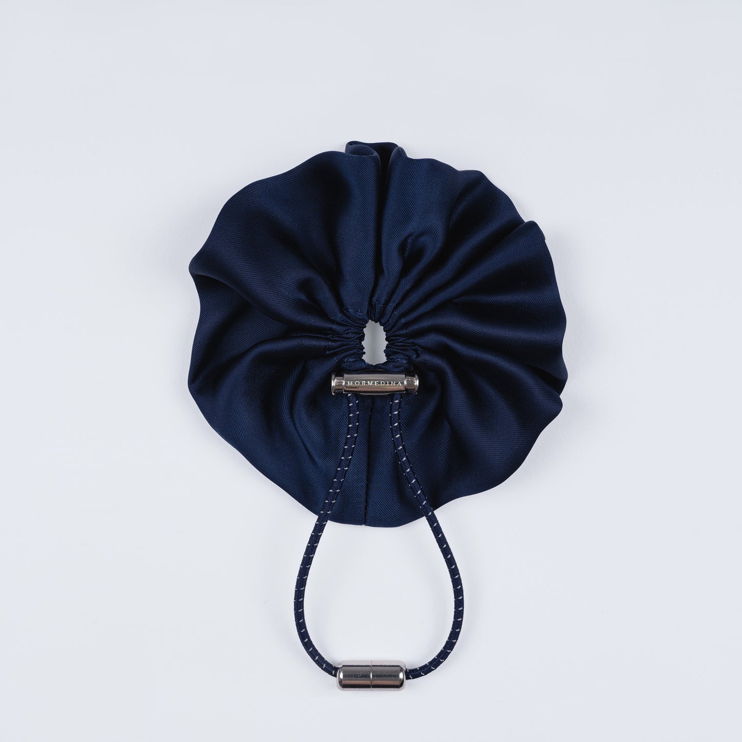 Night blue silk scrunchie displayed closed on a white background, highlighting its smooth texture and unique fastener.