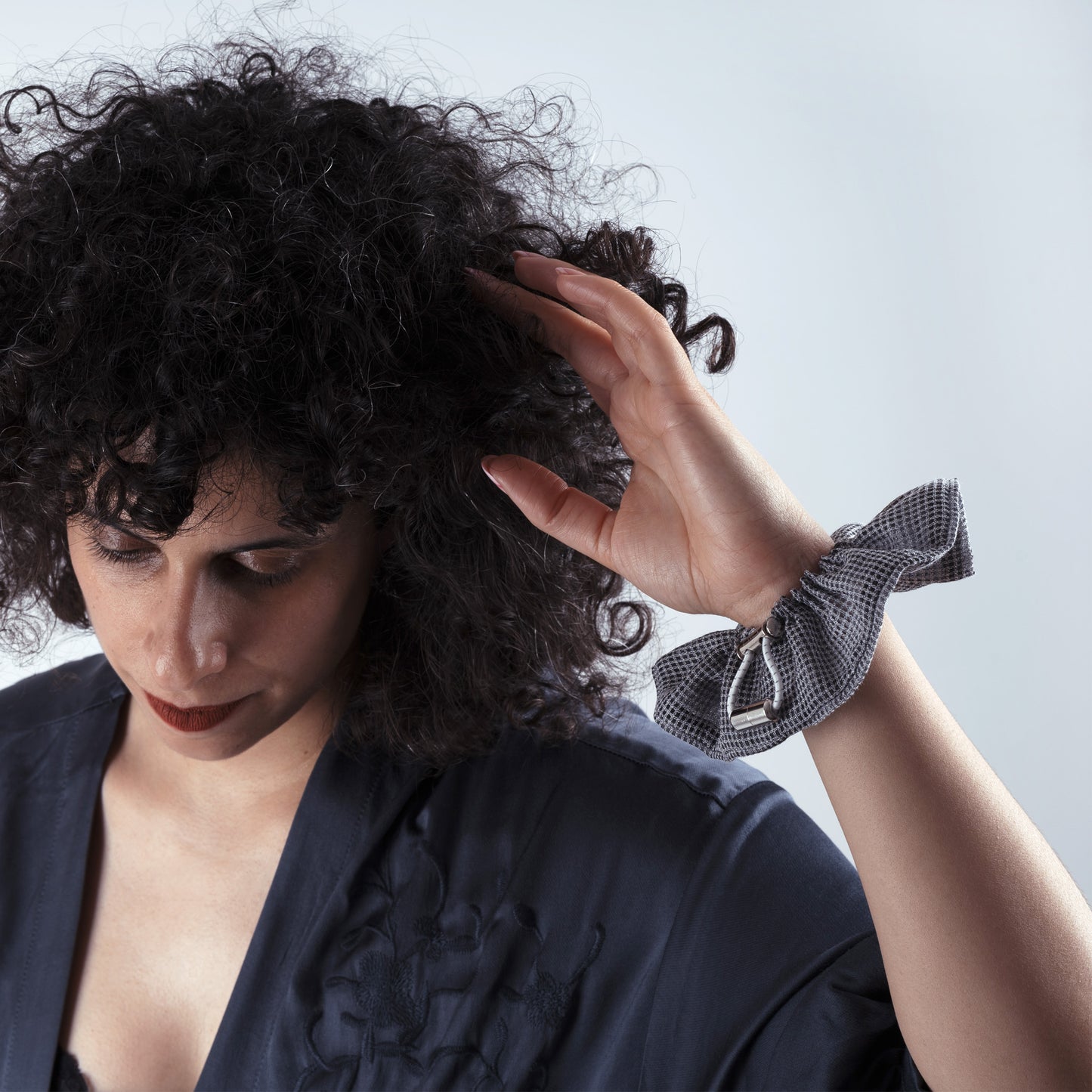 Model wearing the gray squares scrunchie on her hand, showing comfort, adjustability, and refined everyday look.