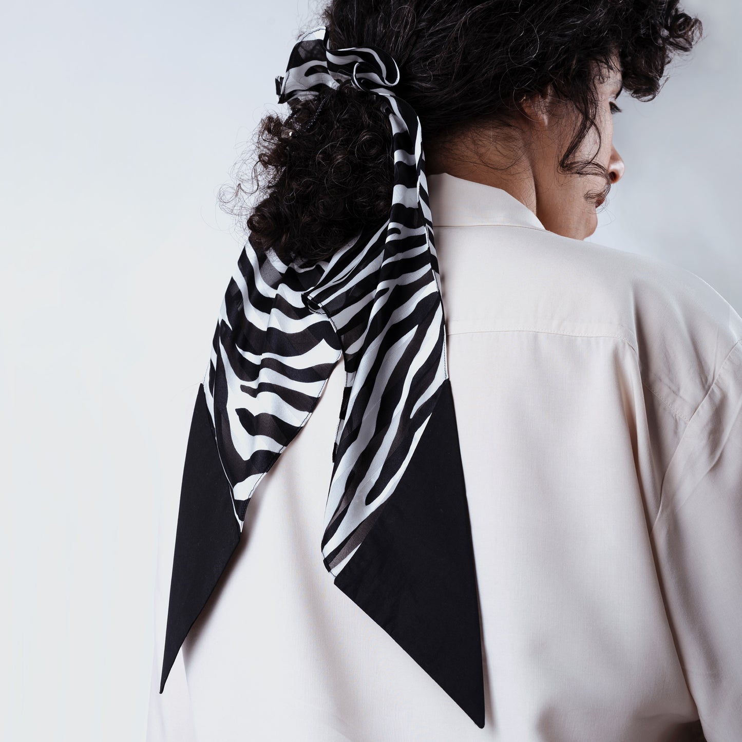 Model wearing a white button-up shirt, showing the zebra print silk scrunchie styled in her hair at the back, highlighting comfort, adjustability, and chic everyday elegance.