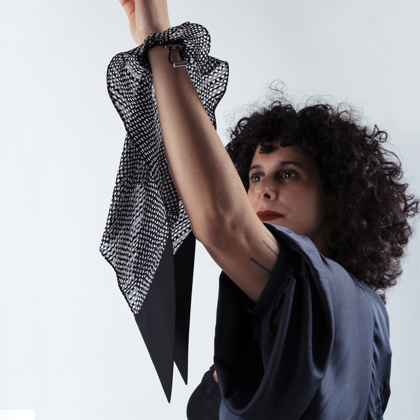 Model placing the black and white dotted silk scrunchie on her hand, highlighting the ease of the adjustable fastener and luxurious soft silk material.