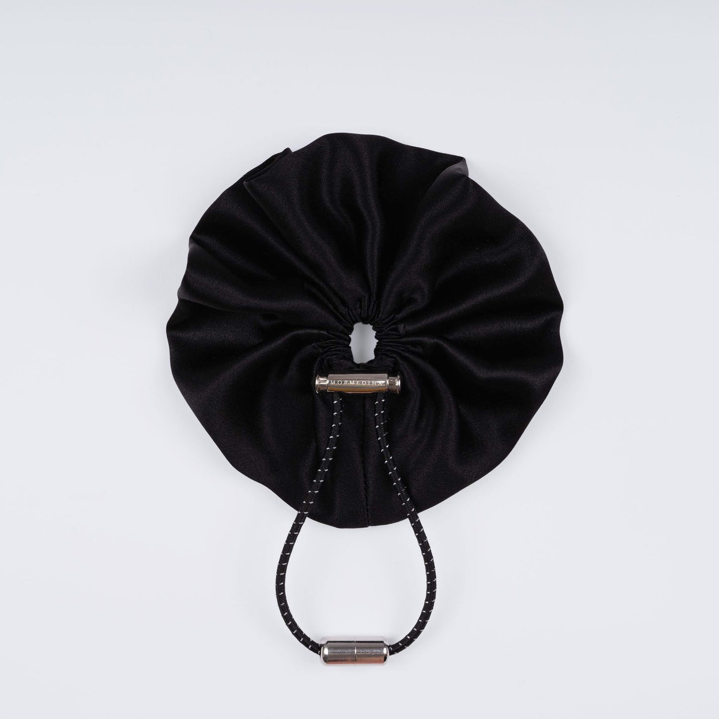 Black silk scrunchie displayed closed on a white background, highlighting its soft texture and unique fastener.
