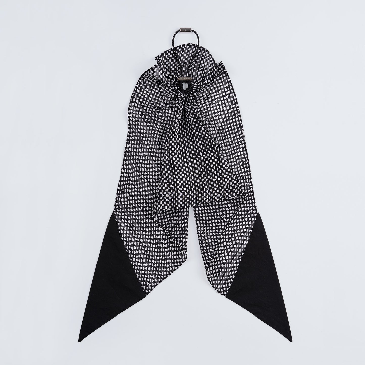 Black and white dotted silk scrunchie displayed closed on a white background, highlighting its unique fastener.