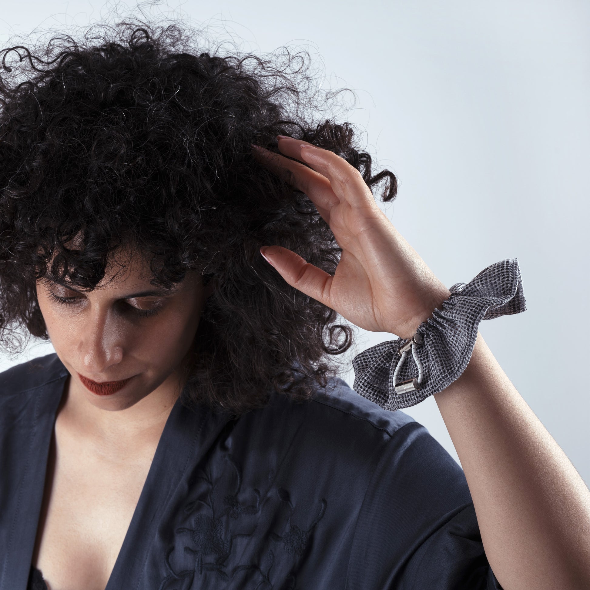 Model wearing the gray squares scrunchie on her hand, showing comfort, adjustability, and refined everyday look.