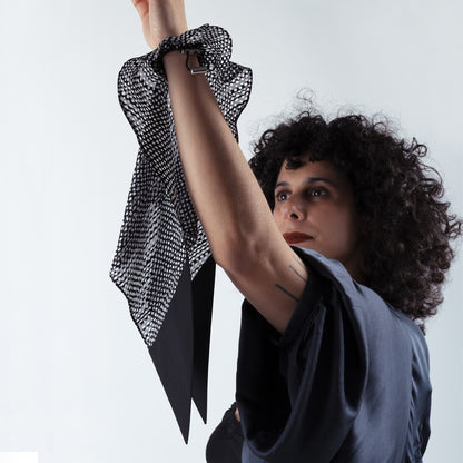 Model placing the black and white dotted silk scrunchie on her hand, highlighting the ease of the adjustable fastener and luxurious soft silk material.