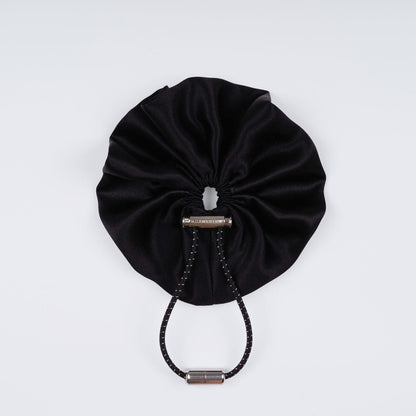 Black silk scrunchie displayed closed on a white background, highlighting its soft texture and unique fastener.