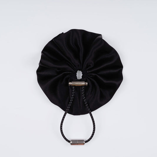 Black silk scrunchie displayed closed on a white background, highlighting its soft texture and unique fastener.