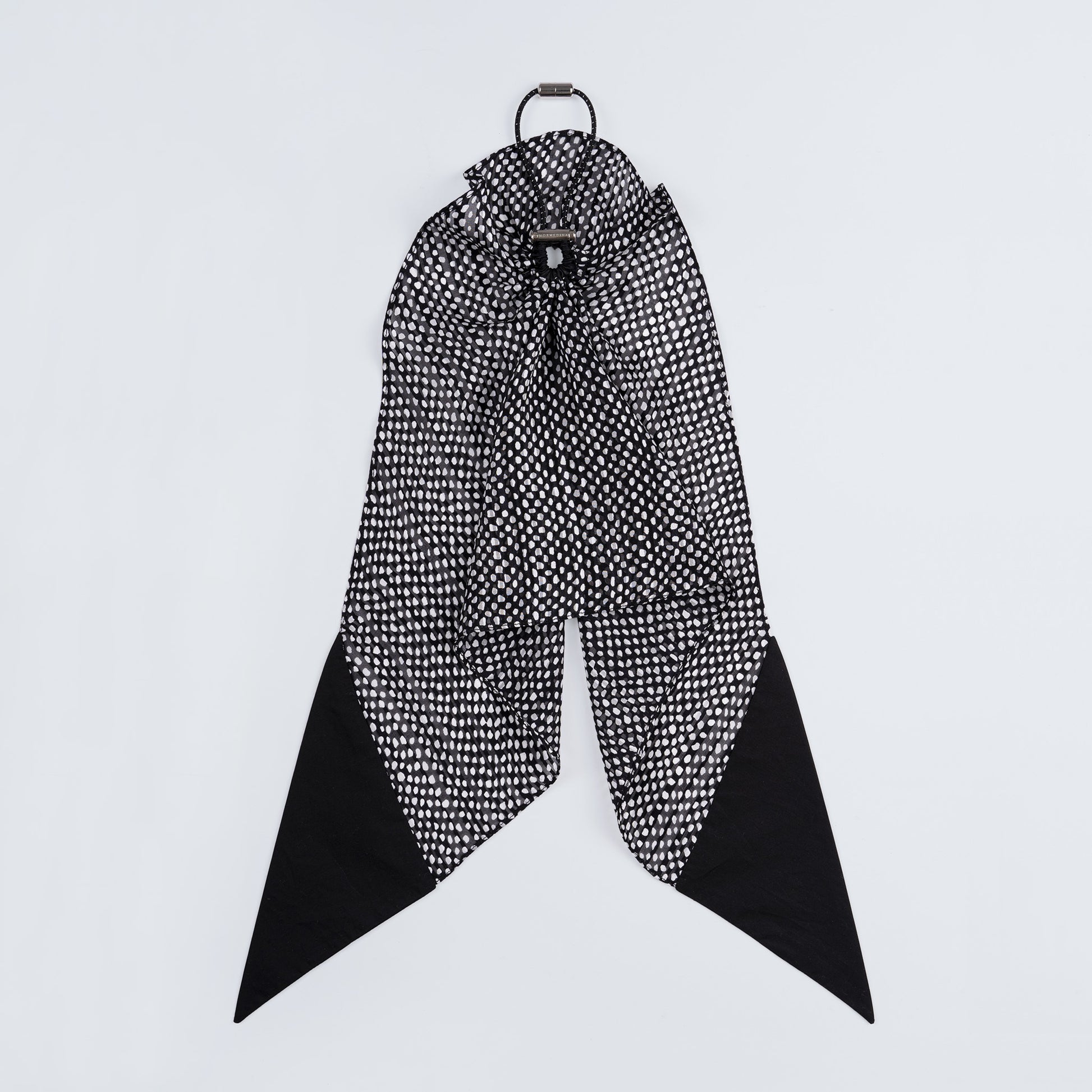 Black and white dotted silk scrunchie displayed closed on a white background, highlighting its unique fastener.