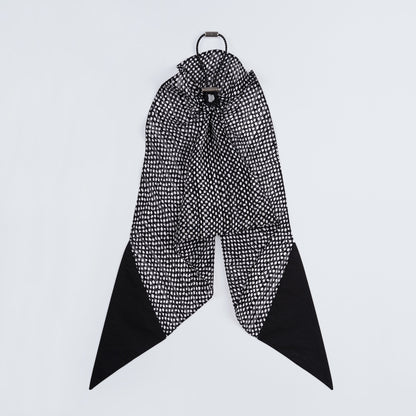 Black and white dotted silk scrunchie displayed closed on a white background, highlighting its unique fastener.